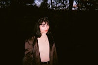 a woman in a brown coat standing in the woods