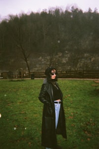 a woman in a black coat standing in a field